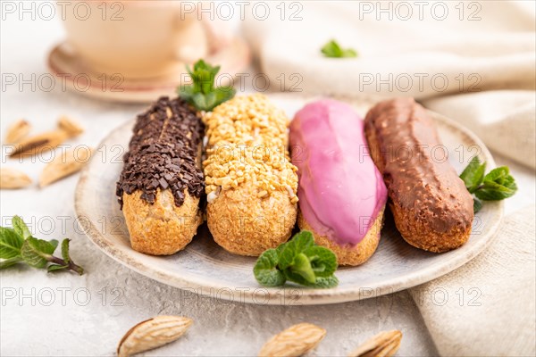 Set of eclair, traditional french dessert and cup of coffee on gray concrete background and linen textile. side view, close up, selective focus, still life. Breakfast, morning, concept