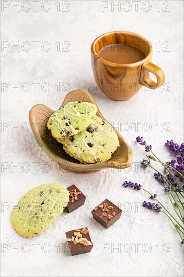 Green cookies with chocolate and mint on leaflike ceramic plate with cup of coffee on gray concrete background. side view, close up