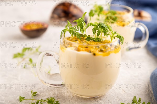 Yogurt with passionfruit and marigold microgreen in glass on gray concrete background with blue linen textile. Side view, close up, selective focus