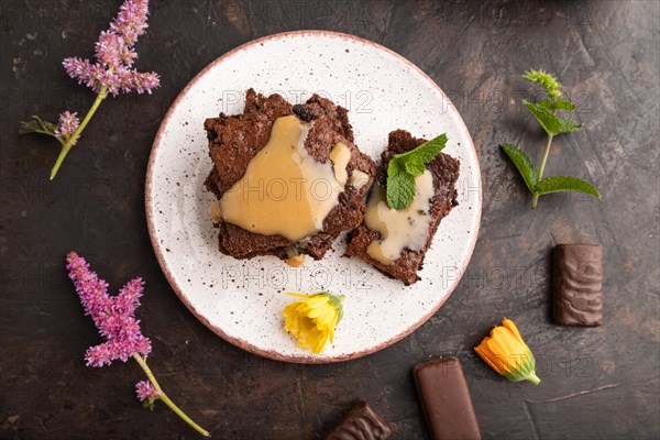 Chocolate brownie with caramel sauce with a cup of coffee on black concrete background. top view, flat lay, close up