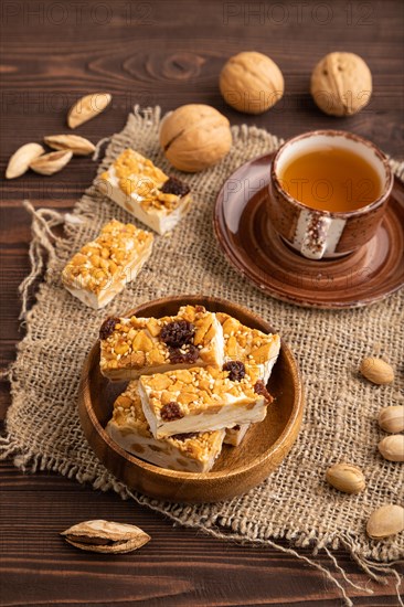 Traditional candy nougat with nuts and sesame with cup of green tea on brown wooden background and linen textile. side view, close up