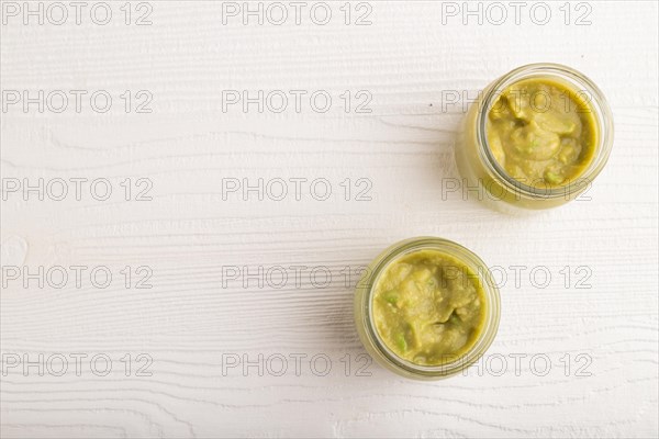 Baby puree with vegetable mix, broccoli, tomatoes, cucumber, avocado infant formula in glass jar on white wooden background. Top view, flat lay, copy space, artificial feeding concept