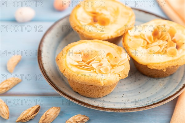 Traditional portuguese cakes pasteis de nata, custard small pies with almonds with cup of coffee on blue wooden background and orange textile. Side view, close up, selective focus