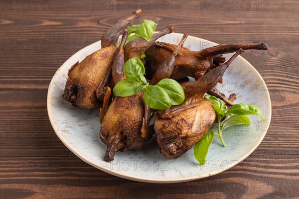 Smoked quails with herbs and spices on a ceramic plate on a brown wooden background. Side view, close up