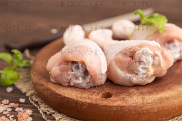 Raw chicken legs with herbs and spices on a wooden cutting board on a brown wooden background and linen textile. Side view, close up, selective focus