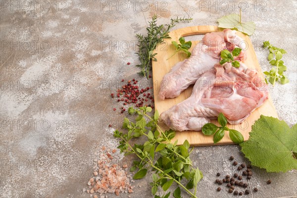 Raw turkey wing with herbs and spices on a wooden cutting board on a brown concrete background. Side view, copy space