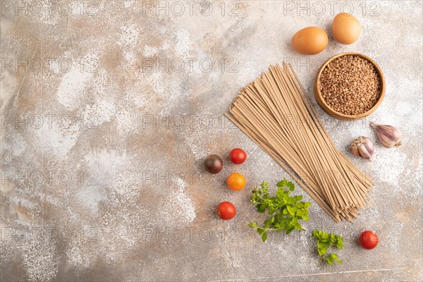 Japanese buckwheat soba noodles with tomato, eggs, spices, herbs on brown concrete background. Top view, flat lay, copy space