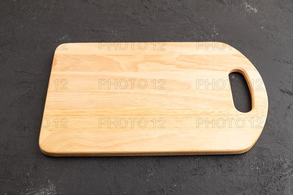 Empty rectangular wooden cutting board on black concrete background. Side view, close up