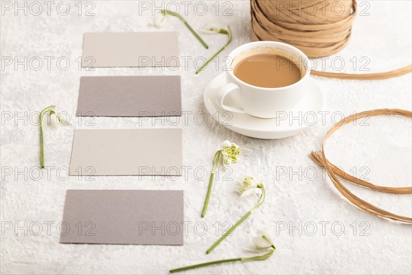 Gray paper business card mockup with spring snowdrop galanthus flowers and cup of coffee on gray concrete background. Blank, business card, side view, copy space, still life. spring concept
