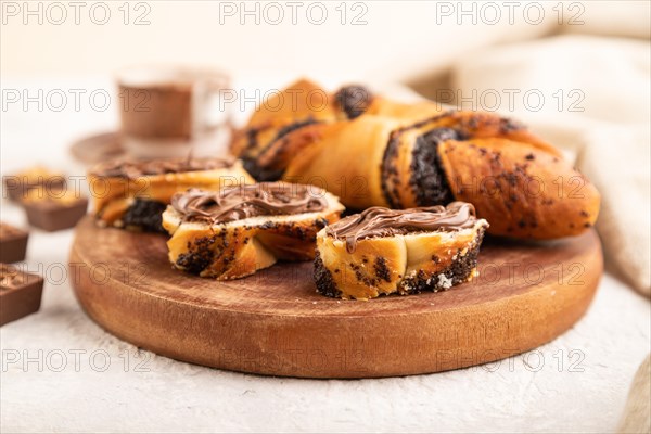 Homemade sweet bun with chocolate cream and cup of coffee on a gray concrete background and linen textile. side view, close up, selective focus
