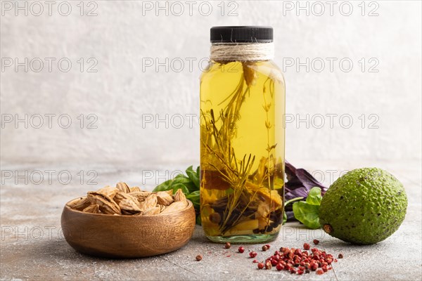 Sunflower oil in a glass jar with various herbs and spices, sesame, rosemary, avocado, basil, almond on a brown concrete background. Side view, copy space
