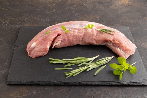 Raw pork meat with herbs and spices on slate cutting board on black concrete background. Side view, close up