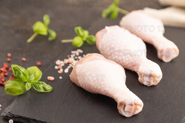 Raw chicken legs with herbs and spices on a black slate cutting board on a black concrete background and linen textile. Side view, close up, selective focus