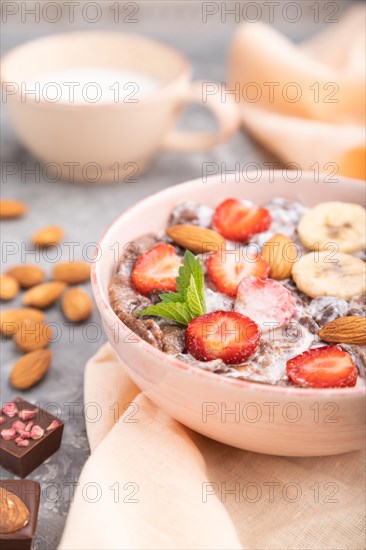 Chocolate cornflakes with milk, strawberry and almonds in ceramic bowl on gray concrete background and orange linen textile. Side view, close up, selective focus