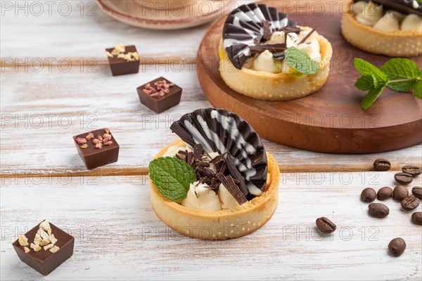 Sweet tartlets with chocolate and cheese cream with cup of coffee on a white wooden background and linen textile. side view, close up
