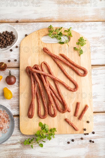 Traditional polish smoked pork sausage kabanos on cutting board with salt and pepper on white wooden background. Top view, flat lay, close up
