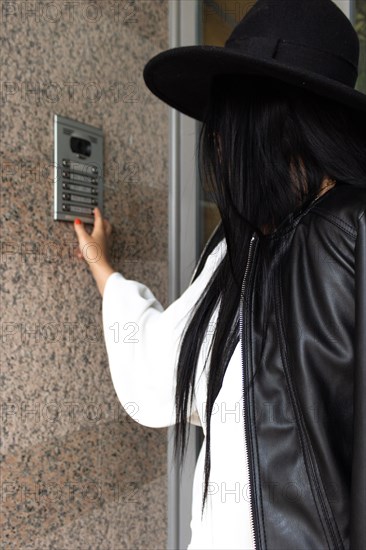 Vertical Side view of unrecognizable woman wearing a hat pushing the button of the intercom of building