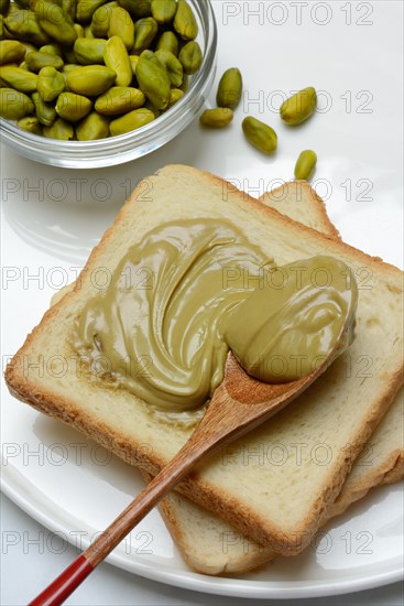 Pistachio cream with a spoon on slices of bread, pistachio in small bowls