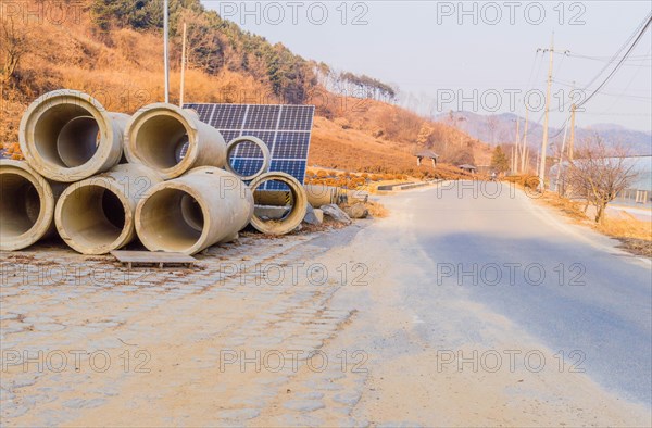 Large concrete culverts in front of array of solar panels on a rural two lane road on overcast winter day
