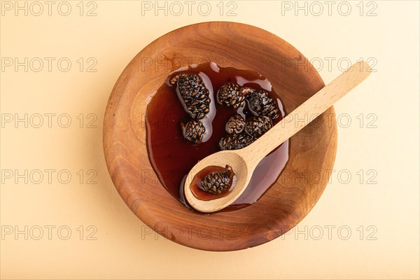 Pine cone jam in wooden bowl on orange pastel background. Top view, flat lay, close up