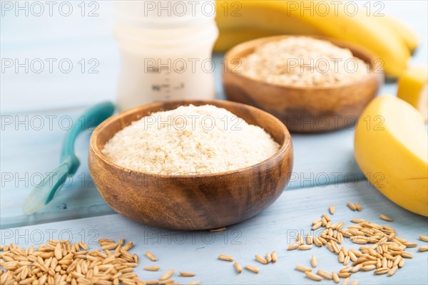 Powdered milk and oatmeal, banana baby food mix, infant formula, pacifier, bottle, spoon on blue wooden background. Side view, selective focus, artificial feeding concept