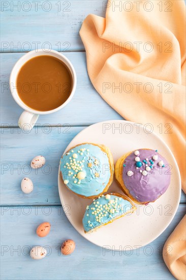 Purple and blue glazed donut and cup of coffee on blue wooden background and orange linen textile. top view, flat lay. Breakfast, morning, concept