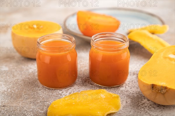 Baby puree with fruits mix, pumpkin, persimmon, mango infant formula in glass jar on brown concrete background. Side view, close up, selective focus, artificial feeding concept
