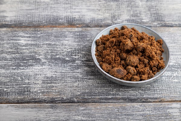 Plate with unrefined brown cane sugar on gray wooden background. side view, copy space