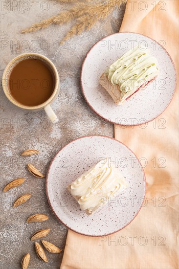 Roll biscuit cake with cream cheese and jam, cup of coffee on brown concrete background and orange linen textile. top view, flat lay, close up