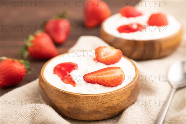 Grained cottage cheese with strawberry jam on brown wooden background and linen textile. side view, close up, selective focus
