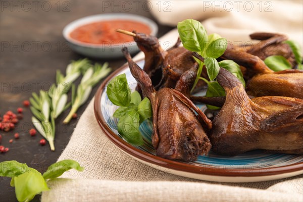 Smoked quails with herbs and spices on a ceramic plate with linen textile on a black concrete background. Side view, close up, selective focus