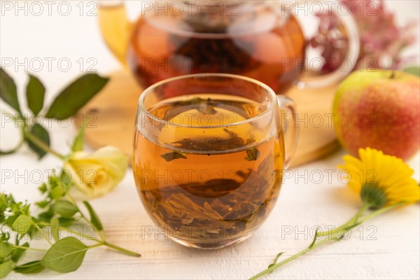 Red tea with herbs in glass teapot on white wooden background. Healthy drink concept. Top view, close up, selective focus