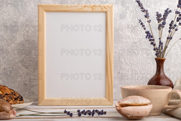 White wooden frame mockup with lavender in ceramic vase, linen textile, cup of coffee and bun on gray concrete background. Blank, vertical orientation, still life