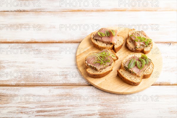 Bread sandwiches with jerky salted meat, sorrel and cilantro microgreen on white wooden background. side view, copy space