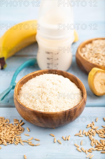 Powdered milk and oatmeal, banana baby food mix, infant formula, pacifier, bottle, spoon on blue wooden background. Side view, selective focus, artificial feeding concept