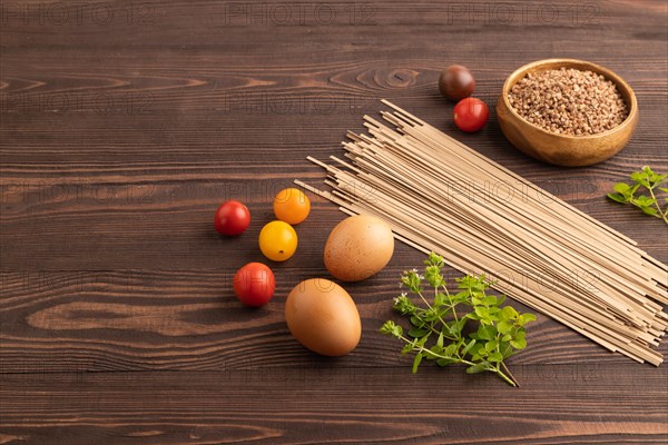 Japanese buckwheat soba noodles with tomato, eggs, spices, herbs on brown wooden background. Side view, copy space