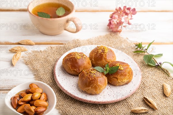 Homemade traditional turkish dessert sekerpare with almonds and honey, cup of green tea on white wooden background and linen textile. side view, close up