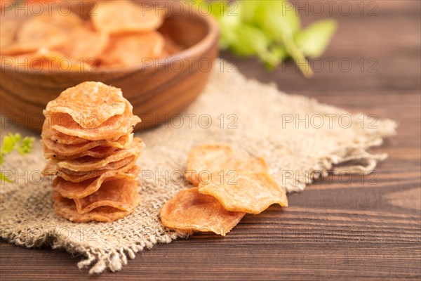 Slices of dehydrated salted meat chips with herbs and spices on brown wooden background and linen textile. Side view, close up, selective focus