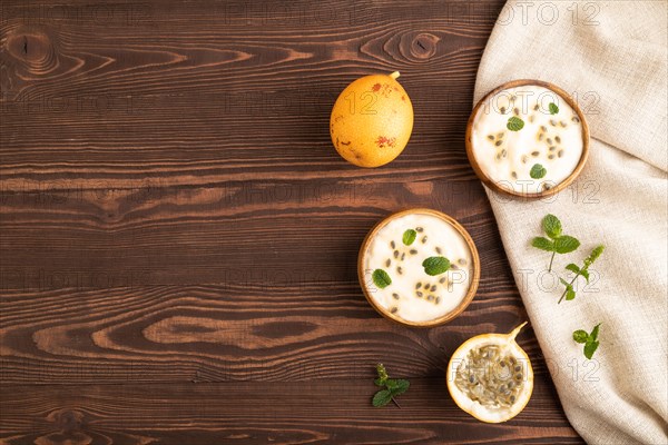 Yoghurt with granadilla and mint in wooden bowl on brown wooden background and linen textile. top view, flat lay, copy space