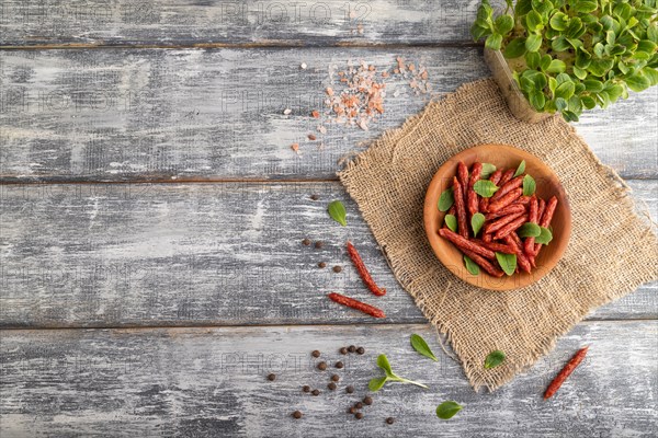 Small smoked sausage with borage microgreen, salt and pepper on gray wooden background and linen textile. Top view, flat lay, copy space