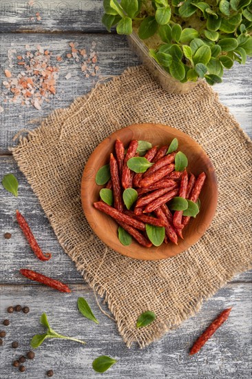 Small smoked sausage with borage microgreen, salt and pepper on gray wooden background and linen textile. Top view, flat lay, close up