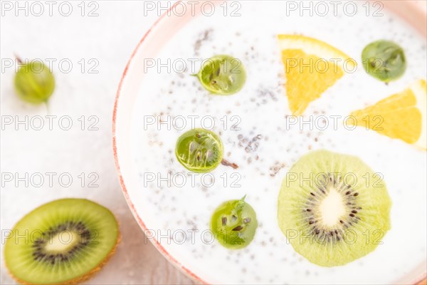 Yogurt with kiwi, gooseberry, chia in ceramic bowl on gray concrete background and orange linen textile. Top view, close up, selective focus