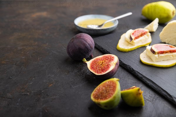 Summer appetizer with pear, cottage cheese, figs and honey on slate board on a black concrete background. Side view, close up, selective focus