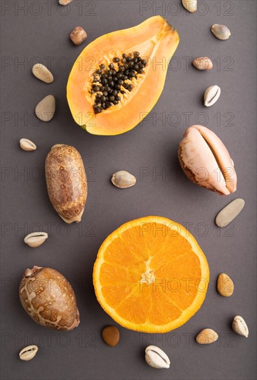 Ripe cut papaya, orange, seashells on gray pastel background. Top view, flat lay, close up. Tropical, healthy food, vacation, holidays concept, minimalism