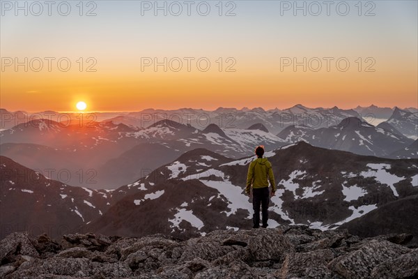Mountaineer enjoying the view, mountain panorama at the summit of Skala at sunset, sun setting behind the mountains, Loen, Norway, Europe