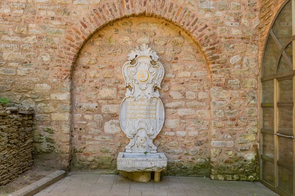 Water fountain with broken taps in shape of coat of arms against brick wall in Istanbul, Tuerkiye
