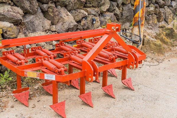 Bright orange plow resting against stone wall in Jeju, South Korea, Asia