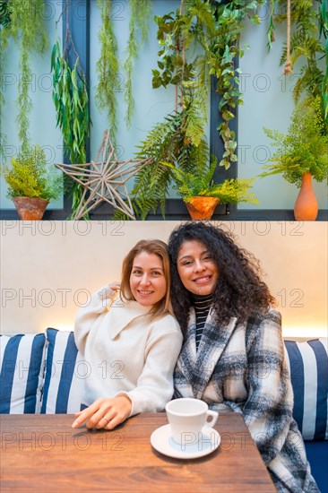 Vertical portrait of two diverse female friends embracing from the back in a cafeteria