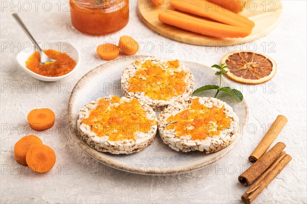 Carrot jam with puffed rice cakes on gray concrete background. Side view, close up