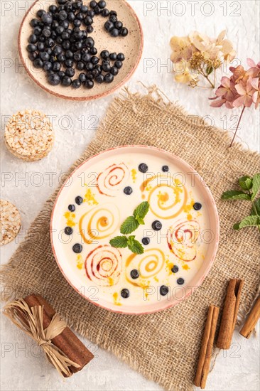 Yoghurt with bilberry and caramel in ceramic bowl on gray concrete background and linen textile. top view, flat lay, close up
